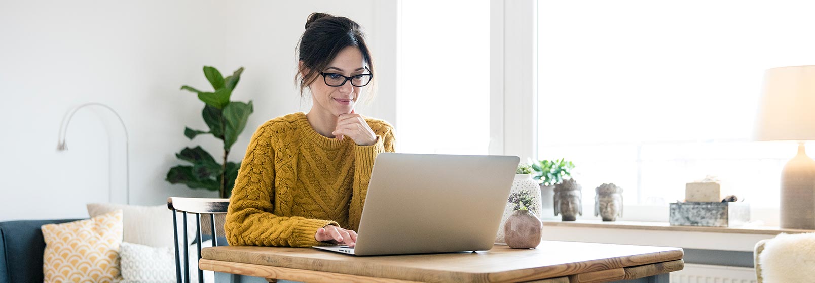 A woman sits at a desk looking at her laptop.